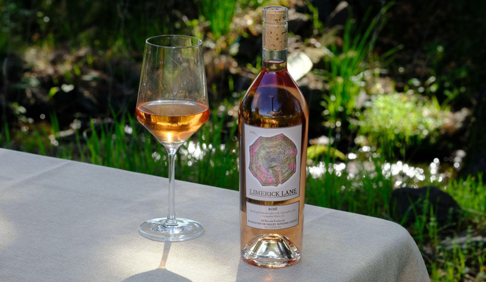 A picture of a half full wine glass with a wine bottle beside it over a table with a white sheet on a garden